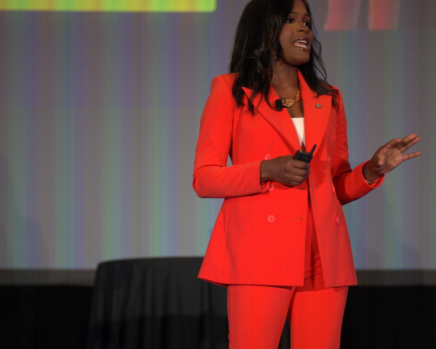 Heather Dowdy delivering a keynote on stage in a signature orange suit