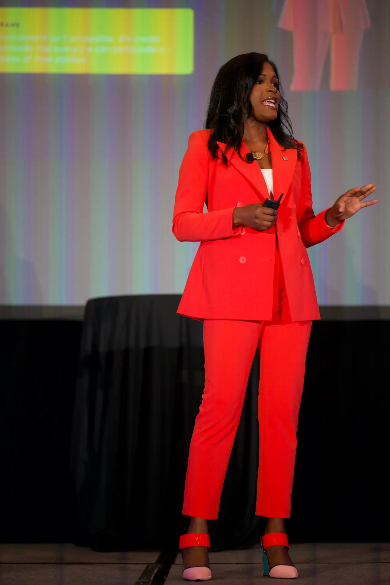 Heather Dowdy delivering a keynote on stage in a signature orange suit